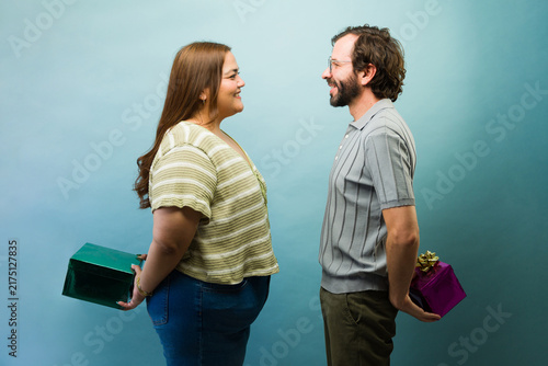 Konstfotografi Happy couple smiling and hiding surprise gifts behind their backs, celebrating a