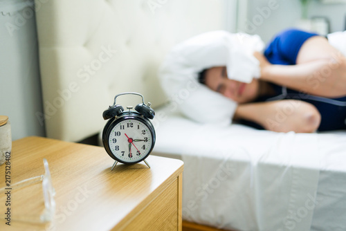 Obraz na plátně Woman trying to sleep, covering head with pillow, disturbed by loud alarm clock