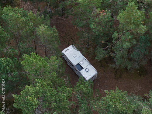 Fotografie Aerial drone top view of white motorhome parked inside dense pine forest surrounded by lush green trees within Estonia natural landscape