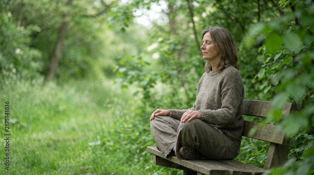 Obraz premium Woman meditating cross legged on park bench in forest setting for mindfulness concept