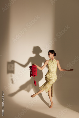 Foto Elegant woman holding red lantern with dramatic shadow in warm light