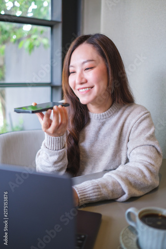 Foto Vertical of a woman holding smart phone and using voice messaging, talking with