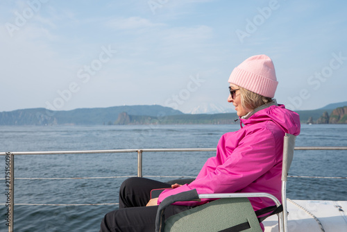 Konstfotografi Woman wearing pink jacket and knit hat enjoys quiet catamaran ride beside Kamchatka coast and Pacific Ocean