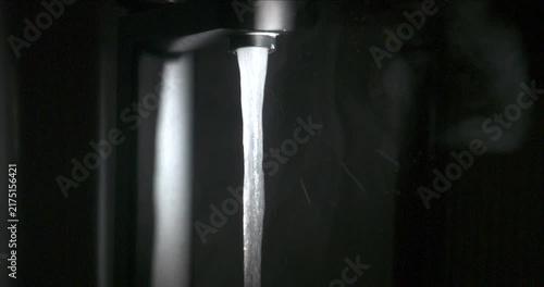 Water flowing from modern chrome faucet on black background