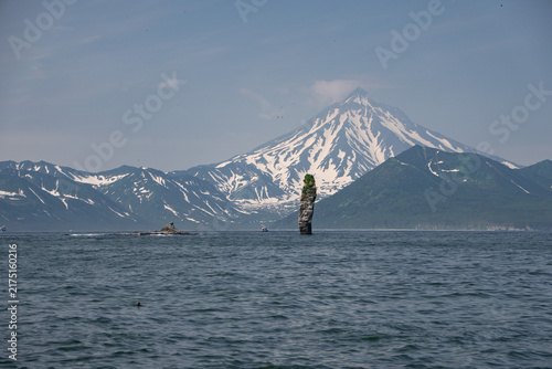 Fotografía Finger sea stack rises from Pacific water against snow-covered Vilyuchinsky Volcano in Kamchatka, Russia