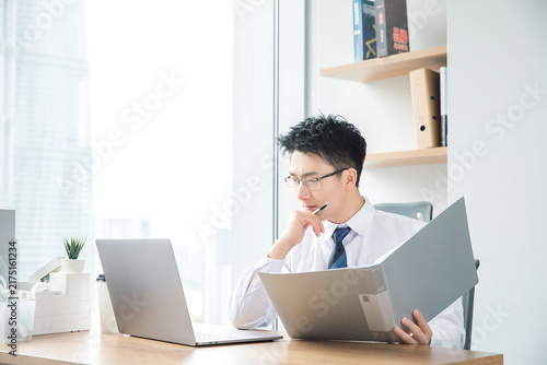 Businessman reviewing documents and working on laptop in modern office