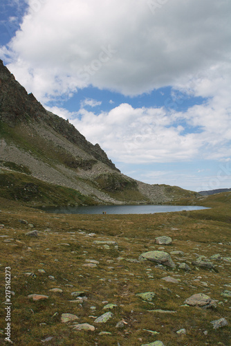 Obraz na plátně Alpiner Bergsee mit zwei Wanderern in karger Hochgebirgslandschaft