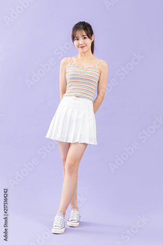 Foto Smiling young woman in striped camisole and white pleated skirt on purple backgr