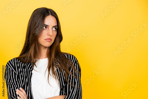 Quadro su tela Young woman with a skeptical expression and arms crossed, thinking or doubting,