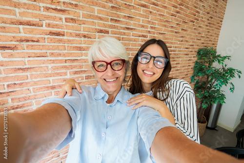 Foto Happy grandmother and granddaughter taking a selfie together at home against a b