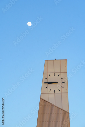 Modern minimalist clock tower under a clear blue sky with a full moon