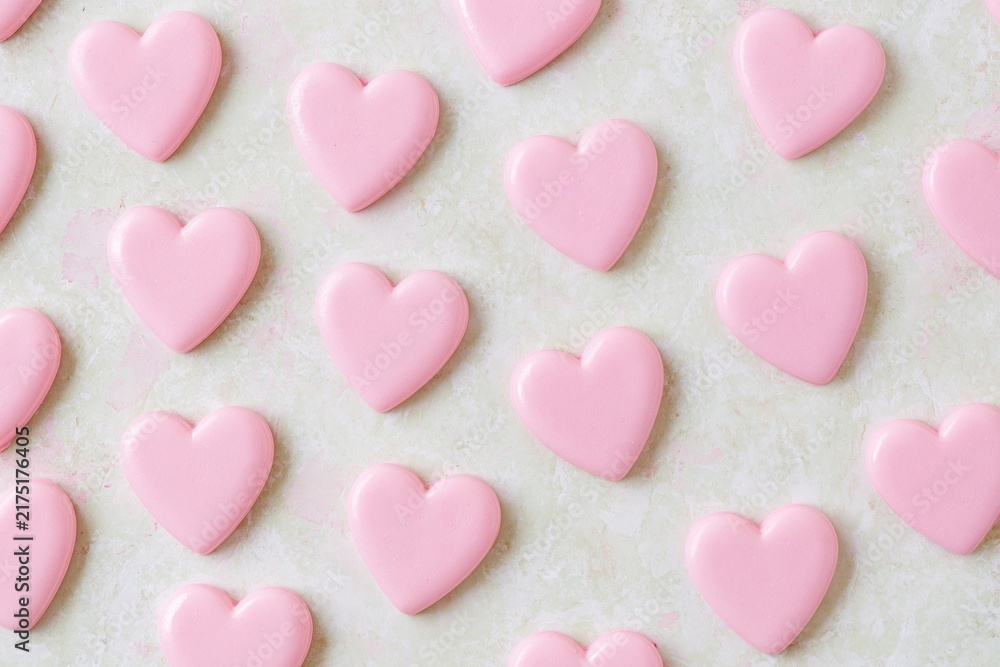 Obraz premium Pink heart shaped candies arranged in scattered pattern on textured neutral surface under soft warm directional light creating romantic festive mood for Valentine's Day celebration