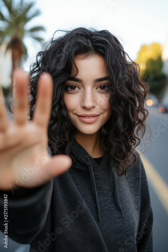 people of ai, dynamic dark-haired woman raising hand in city street, photorealistic