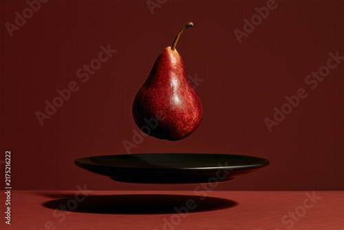 Floating pear above plate in vibrant red hue