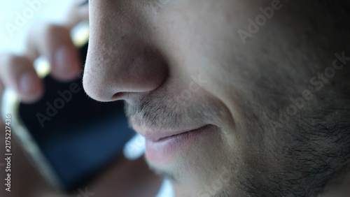 Close up male mouth speaking by smartphone near window with day light. Handsome bearded guy talking on phone at apartment. Young man having conversation on cellphone at office. Slow motion