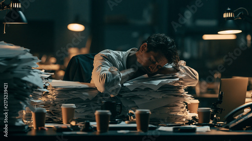 Tired office worker resting on paperwork, surrounded by coffee cups, in dimly lit workspace, high contrast cinematic style, stress and exhaustion visible
