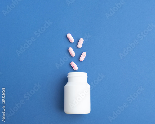 Pink pills with spilled out of a plastic jar. Medicine capsules on blue background with copy space. Ideal for healthcare, pharmaceutical treatments, and medical medication industries.