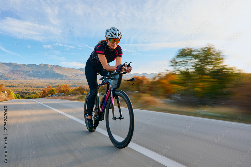 Naklejka premium Female Cyclist Speeding on Road Bike Through Autumn Mountains During Time Trial Training