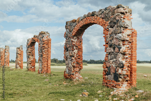 Foto Crumbling brick-and-stone arches stand across a grassy rural field beneath a bri