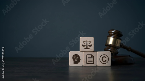 Legal concept of intellectual property rights depicted by wooden blocks with copyright icons and a judge gavel on a dark wooden table.
