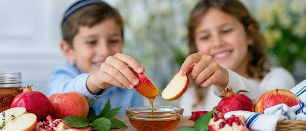 Obraz premium Smiling children dipping apples together beside pomegranate, rosh hashanah family food ritual for a sweet jewish new year