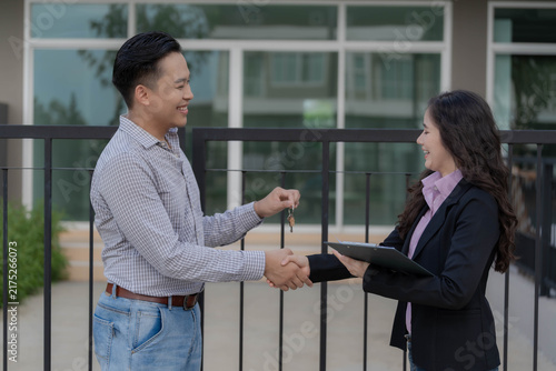 Female real estate agent handing house keys to young male customer in front of new property