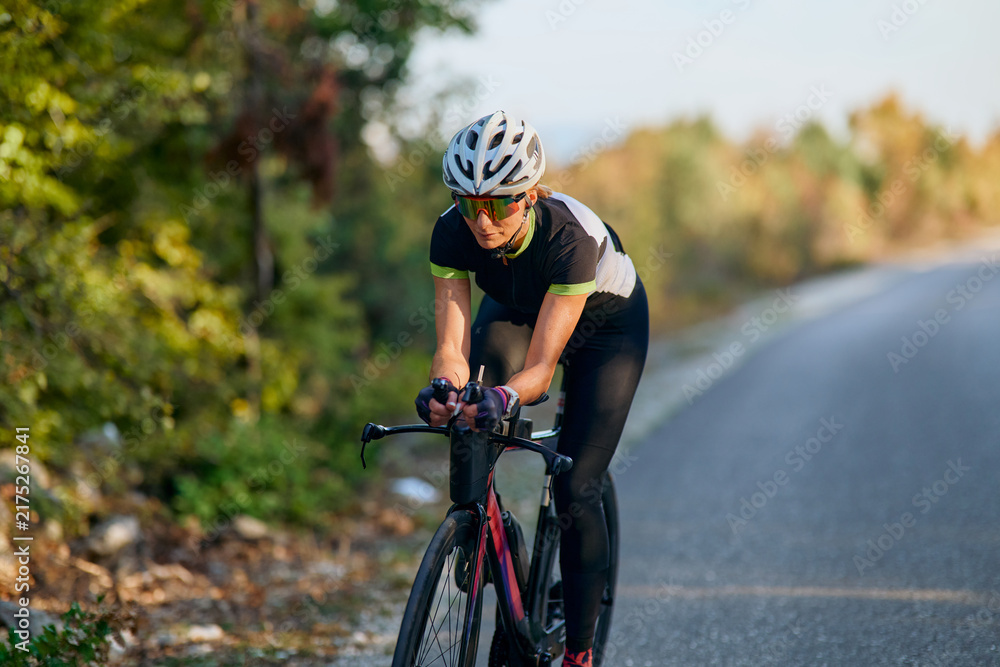 Naklejka premium Female Cyclist Riding Road Bike On Rural Road Training Outdoors In Cycling Kit