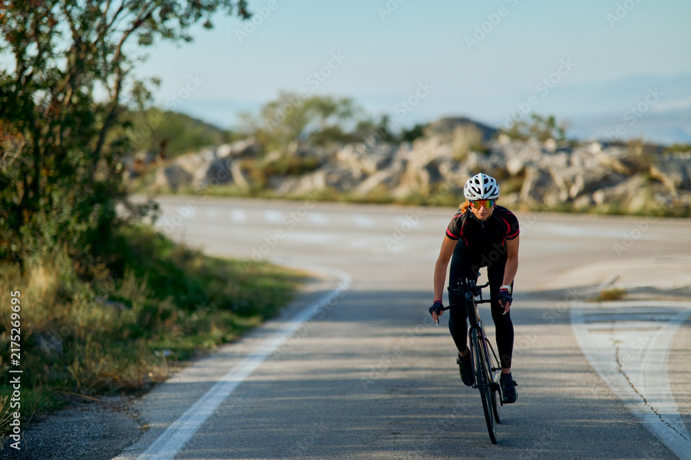 Obraz premium Female Cyclist Riding Road Bike on Winding Country Road During Morning Training Session