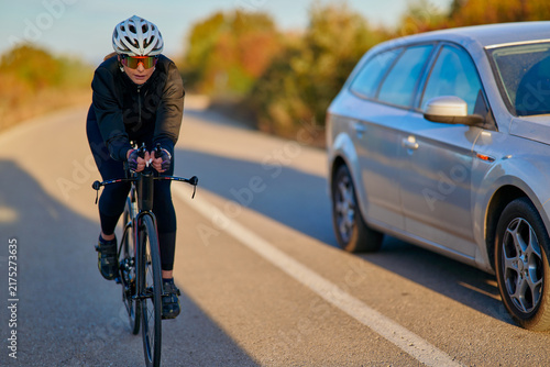 Female Cyclist Riding a Road Bike Alongside a Passing Car on a Country Road in Autumn