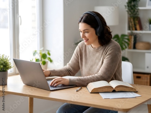 A young woman wearing headphones studies intently on her laptop at a desk