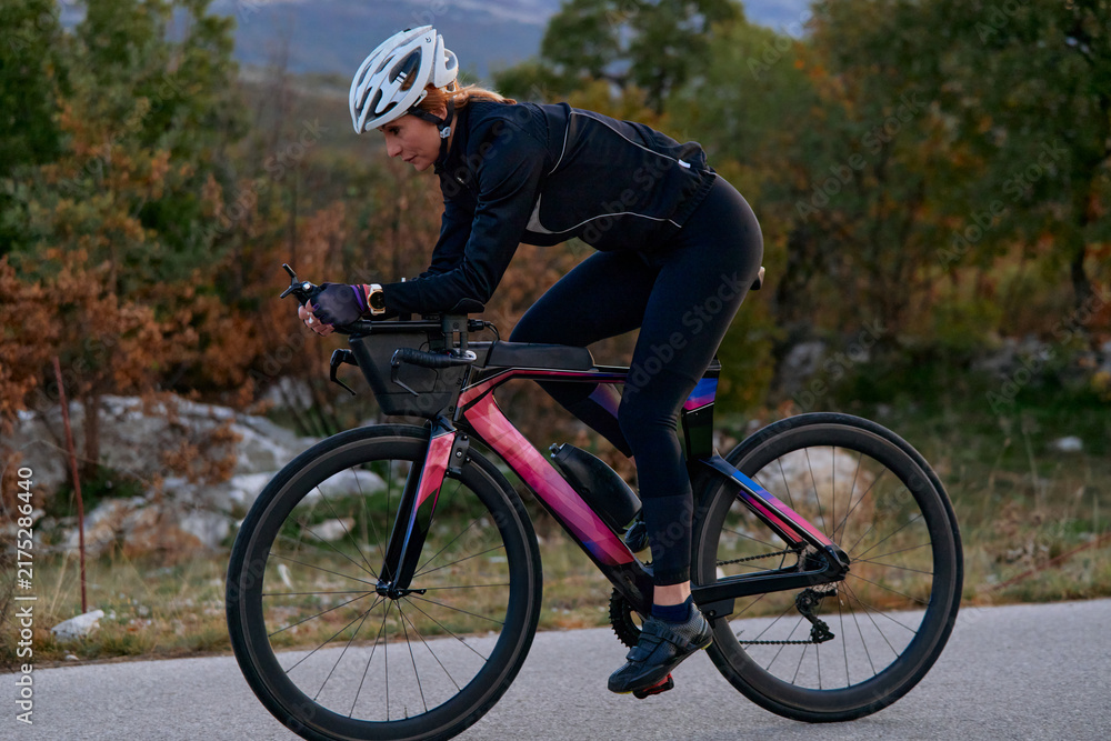Naklejka premium Female Cyclist Training on Road Bike at Dusk Wearing Helmet and Cycling Gear