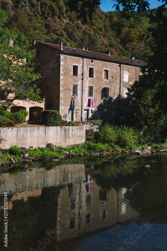 Old stone house reflected in a calm river with laundry hanging outside