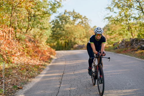 Female Cyclist Training On Quiet Country Road Through Autumn Forest For Fitness And Endurance