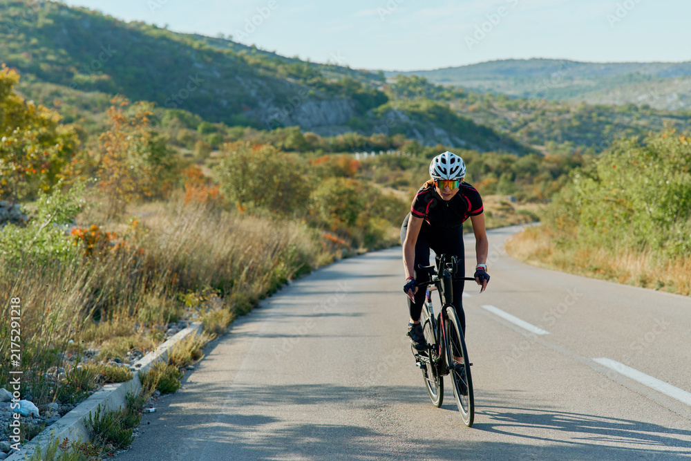 Fototapeta premium Road Cyclist Training on Scenic Rural Highway Surrounded by Hills and Autumn Vegetation