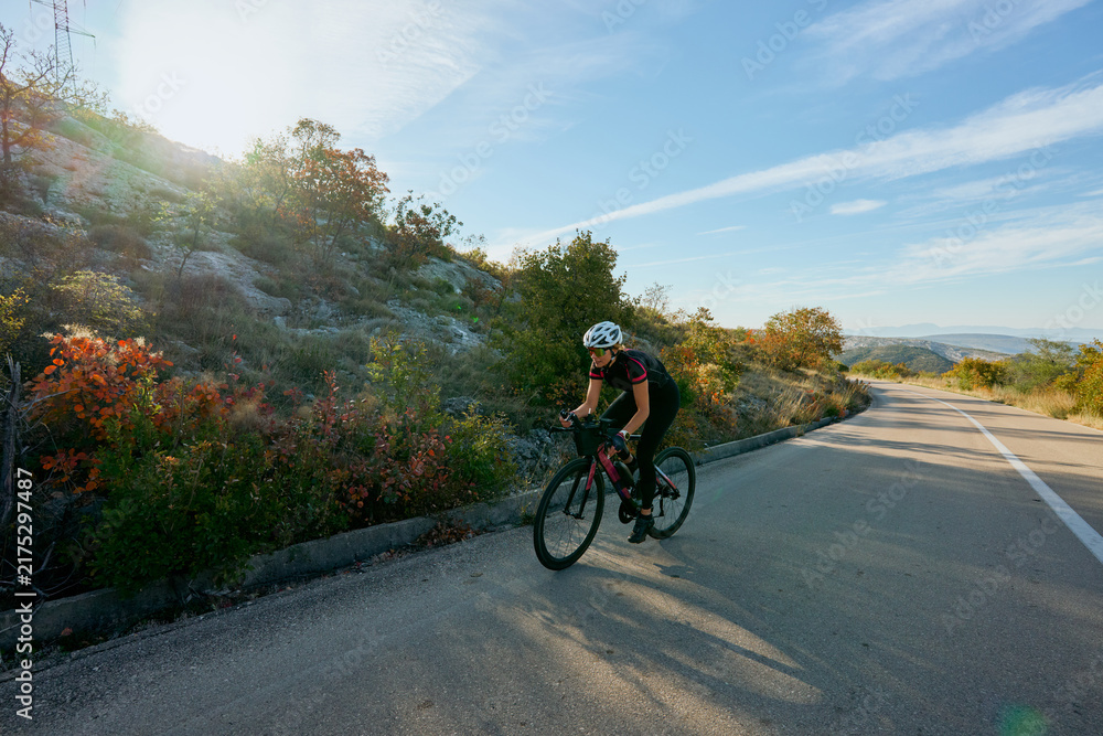 Fototapeta premium Female Cyclist Training on Scenic Road Through Hills at Sunrise Outdoor Cycling and Fitness Lifestyle