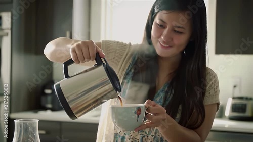 Young woman pouring hot water from electric kettle into a ceramic cup in home kitchen