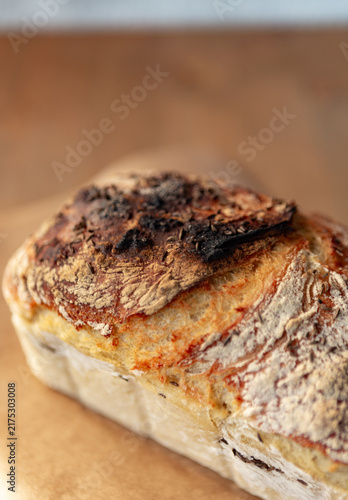 Freshly baked artisanal sourdough bread loaf sprinkled with caraway seeds, resting on baking paper over a wooden background, rustic bakery style.