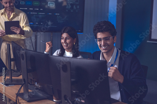 Technology team celebrates success while working at desktop computers in a modern office, showing collaboration, software development, digital innovation, teamwork and positive results