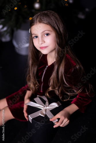Close up of cute little girl holding Christmas gift box sitting near Christmas tree