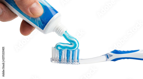 Hand squeezing fresh blue and white striped toothpaste onto soft plastic bristles of manual toothbrush