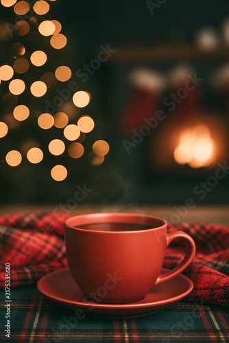 Red cup of tea on plaid fabric near fireplace