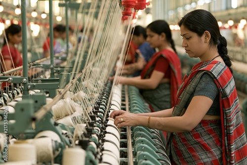Indian female textile worker in traditional saree operating large industrial weaving loom
