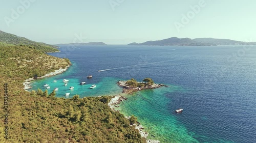 Aerial view of luxury yachts anchored in a turquoise bay surrounded by a rocky coastline and green forest. Summer seaside vacation scene. Drone view of the yachts.