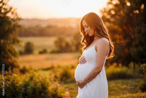 Beautiful Pregnant Woman Standing in Nature Field Holding Belly at Golden Hour Sunset