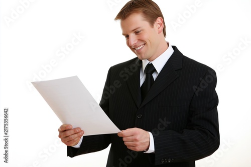 Smiling businessman in a black suit holding and reading a document against a plain white background