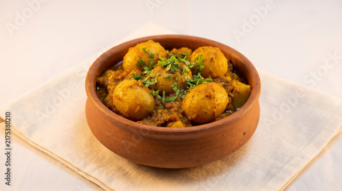 Traditional Niramish Aloor Dum topped with fresh coriander leaves in a rustic clay bowl, white background,