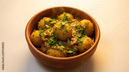 Traditional Niramish Aloor Dum topped with fresh coriander leaves in a rustic clay bowl, white background,