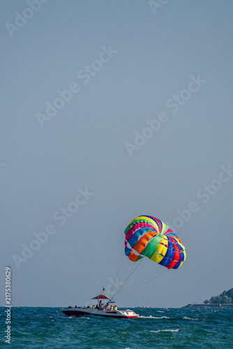 Fotografía A motorboat tows a colorful rainbow parasail across the open sea under a clear blue sky
