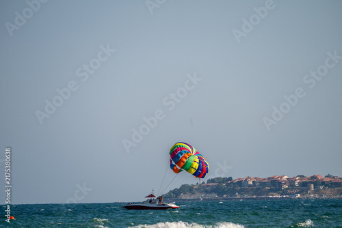 Fotografía A motorboat tows a colorful rainbow parasail across the open sea under a clear blue sky