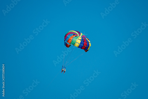 фотографія A colorful parasail carrying two people soars high in the clear blue sky
